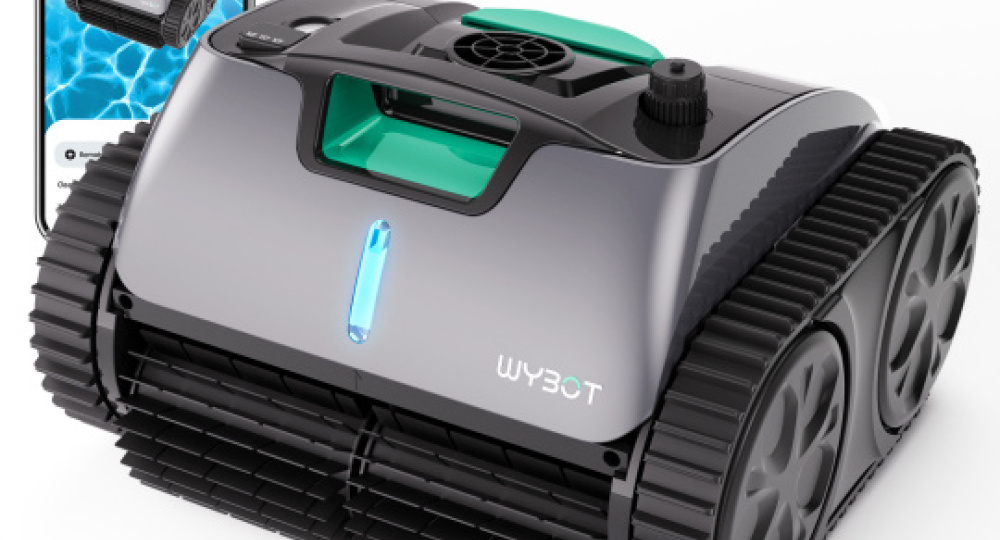 Kompaktowy, czarny robot do czyszczenia basenu z bieżnikami przypominającymi zbiornik, oznaczony WYBOT, znajduje się na białej powierzchni. W tle widoczny jest smartfon wyświetlający aplikację z obrazem odkurzacza basenowego.
