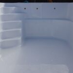 Czysty, pusty, biały basen z zakrzywionymi schodami po lewej stronie i gładkimi ścianami, odbijającymi światło. Na drugim końcu ściany basenu widoczne są trzy okrągłe otwory.