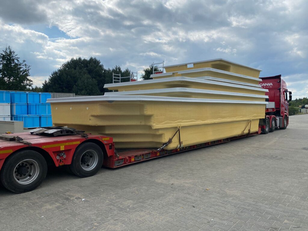 Duży żółty basen jest ułożony na czerwonej przyczepie płaskiej przymocowanej do czerwonej półciężarówki