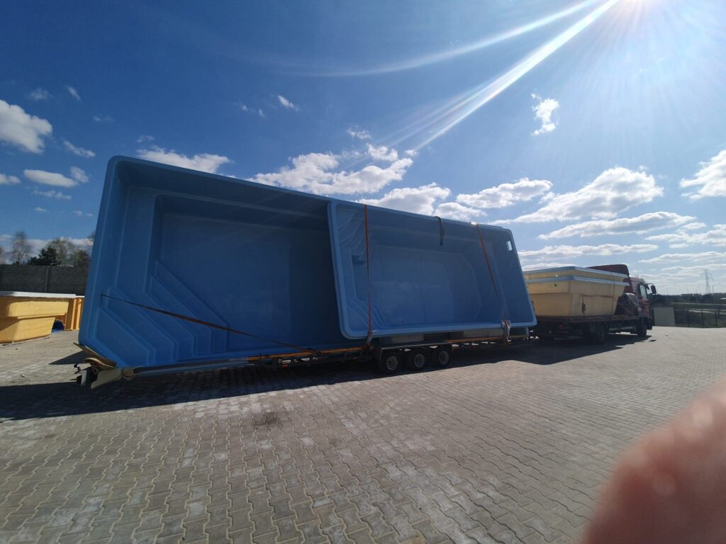 Duży niebieski basen jest zamocowany na przyczepie płaskiej przymocowanej do ciężarówki