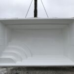 Duży, pusty prostokątny biały basen z włókna szklanego z wbudowanymi zakrzywionymi schodami po jednej stronie.