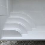 Zbliżenie na białe, zakrzywione stopnie wewnątrz pustej obudowy basenu, z zaśnieżoną scenerią zewnętrzną widoczną w tle.