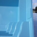 Zbliżenie na wnętrze jasnoniebieskiego pustego basenu z wbudowanymi schodami, na zewnątrz w słoneczny dzień. Na zewnątrz basenu widoczny jest śnieg.