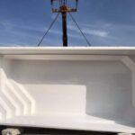 Duża, biała, prostokątna powłoka basenu z włókna szklanego jest podnoszona przez dźwig.