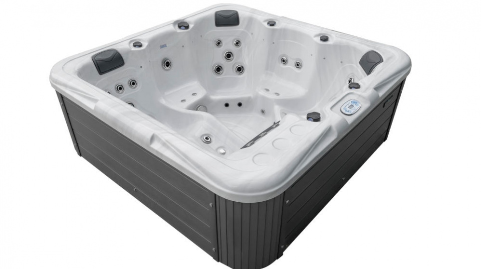 Duża, nowoczesna zewnętrzna wanna z hydromasażem z białym wnętrzem, wieloma wbudowanymi siedzeniami, kilkoma dyszami wodnymi, czarnymi zagłówkami i ciemnoszarymi panelami zewnętrznymi. Elementy sterujące i uchwyty na kubki są widoczne na krawędzi.