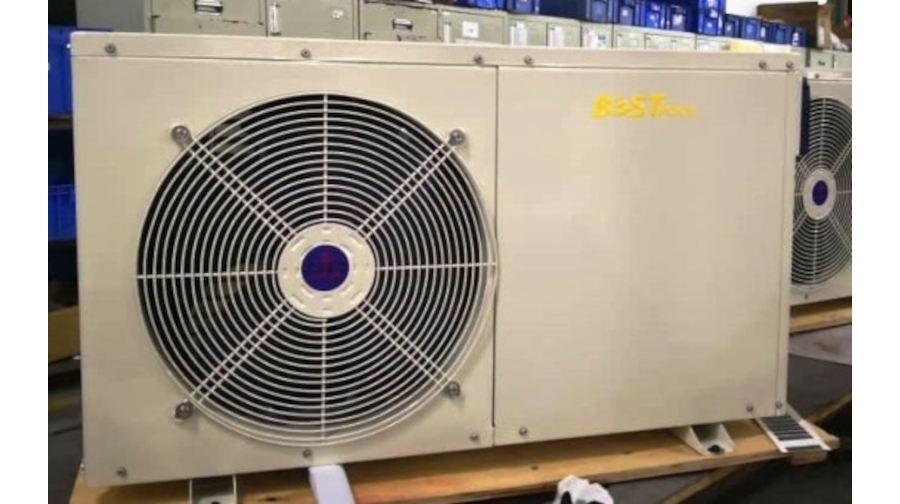 Beżowy klimatyzator przemysłowy z dużym czarnym grillem wentylatora po lewej stronie i żółtym logo BEST po prawej, umieszczony na drewnianej palecie w pomieszczeniu.