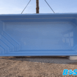 Duża, pusta, jasnoniebieska powłoka basenu z włókna szklanego jest zawieszona na zewnątrz, gotowa do instalacji.